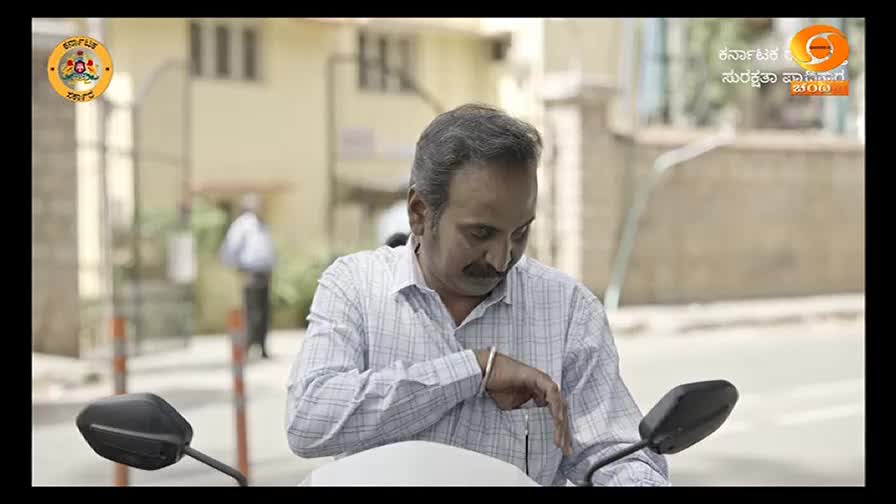 A man on a scooter, wearing a light-colored shirt, looks down at his wrist. He seems to be checking the time, perhaps before a segment on DD Chandana.
