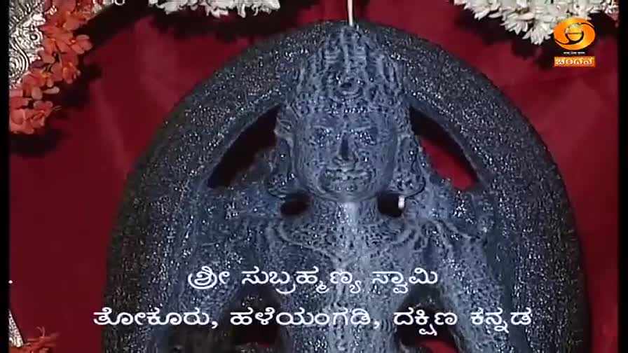 A dark, textured sculpture of a deity is centered, framed by a red backdrop and floral accents. Below, text in Kannada identifies the location as Sri Subrahmanya Swamy.
A dark, textured sculpture of a deity is centered, framed by a red backdrop and floral accents. Below, text in Kannada identifies the location as Sri Subrahmanya Swamy.