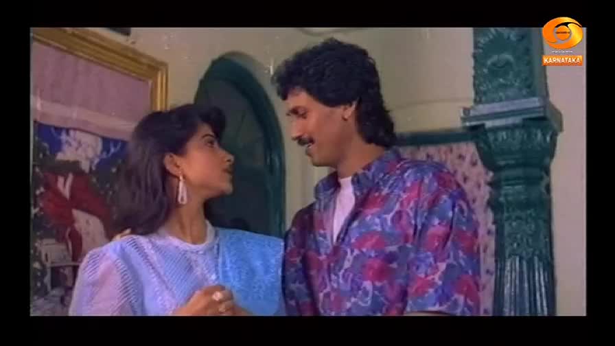 A man in a patterned shirt gazes at a woman wearing a light blue top, both of them in a scene from what looks like a DD Chandana production. They appear to be in a close, intimate moment, possibly a scene from a film made in India.
A man in a patterned shirt gazes at a woman wearing a light blue top, both of them in a scene from what looks like a DD Chandana production. They appear to be in a close, intimate moment, possibly a scene from a film made in India.