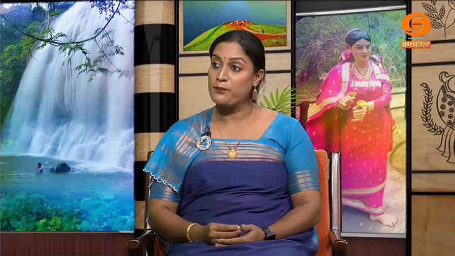 DD Chandana, dressed in a blue saree, sits in a studio set, speaking to someone off-screen. Behind her, a waterfall and a portrait of a woman in traditional Indian attire are displayed.
DD Chandana, dressed in a blue saree, sits in a studio set, speaking to someone off-screen. Behind her, a waterfall and a portrait of a woman in traditional Indian attire are displayed.