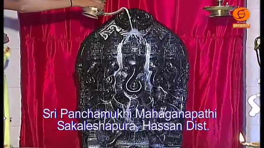 A stream of milky liquid pours from a small vessel, cascading down the surface of a dark, intricately carved statue. The scene is broadcast on DD Chandana, a television channel in India.
A stream of milky liquid pours from a small vessel, cascading down the surface of a dark, intricately carved statue. The scene is broadcast on DD Chandana, a television channel in India.