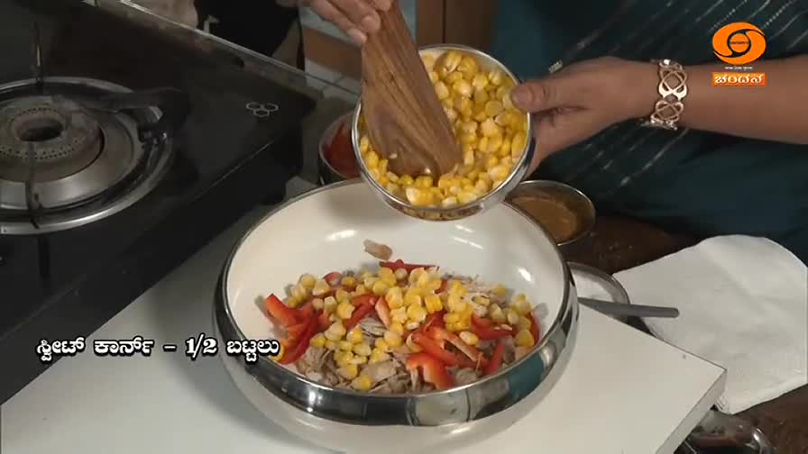 Golden kernels of corn are being poured from a bowl into a larger one, already filled with red peppers and other ingredients. A woman in a green top and a bracelet is carefully using a wooden spoon.
Golden kernels of corn are being poured from a bowl into a larger one, already filled with red peppers and other ingredients. A woman in a green top and a bracelet is carefully using a wooden spoon.