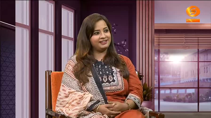 DD Chandana sits in a studio chair, smiling as she speaks, her hands clasped in her lap. The backdrop features a window with a view of a building and a logo in the top right corner.
DD Chandana sits in a studio chair, smiling as she speaks, her hands clasped in her lap. The backdrop features a window with a view of a building and a logo in the top right corner.