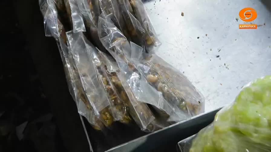 Bundles of dried fish, likely for sale at a market, lie in clear plastic. A logo for DD Chandana, Karnataka's state television, appears in the corner.