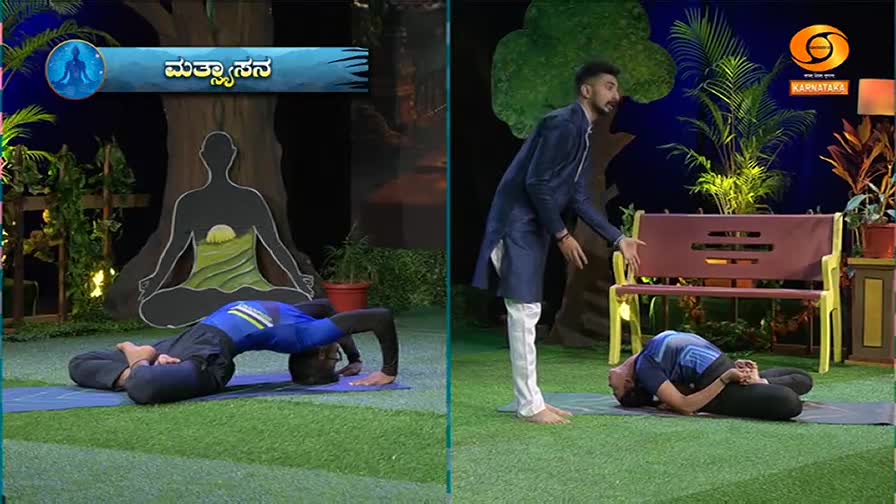 On the left, a man in a blue and black outfit arches his back on a yoga mat, his head touching the ground. To the right, another man in similar attire lies on his back, knees bent, while a man in a dark blue kurta and white pants leans in, gesturing. This is part of a segment on DD Chandana, likely demonstrating a yoga pose.