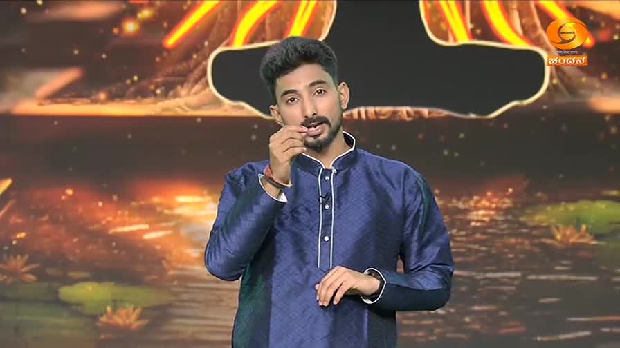 A man in a deep blue kurta gestures with his fingers. The background behind him glows with warm, abstract lights, hinting at a stage production.