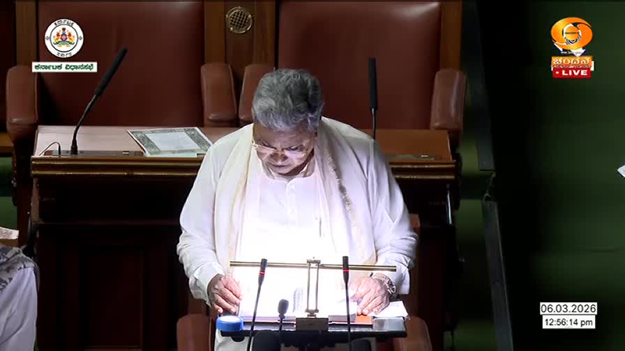 A man in a white kurta stands at a podium, his hands resting on papers. The DD Chandana logo is visible in the corner, indicating this is a live broadcast from India.