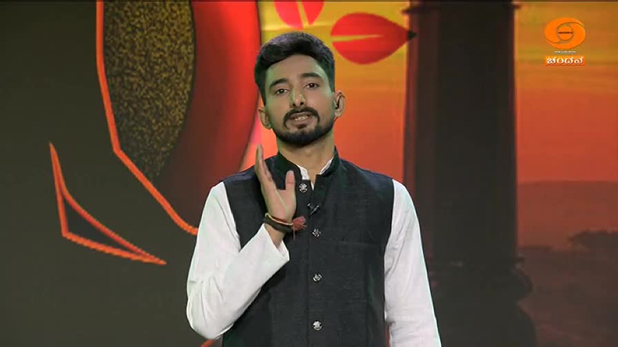 A man in a white kurta and dark vest speaks with his hand raised. Behind him, the DD Chandana logo glows against a warm, abstract backdrop.