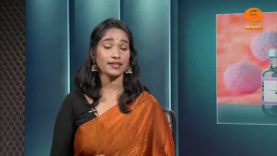 A woman in an orange sari speaks on a set, with a graphic of a vaccine vial and cells behind her. This is a segment from DD Chandana.