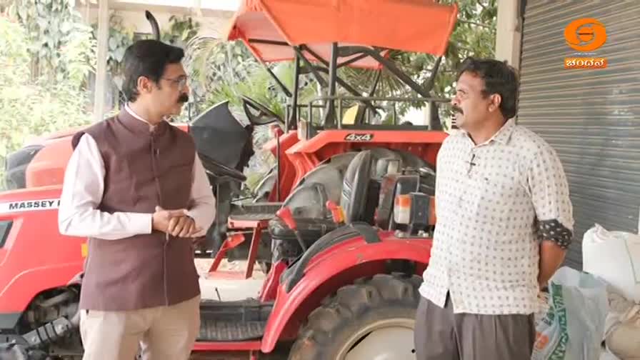 Two men stand near a red Massey Ferguson tractor, one in a brown vest and the other in a patterned shirt. A DD Chandana logo appears in the upper right corner.