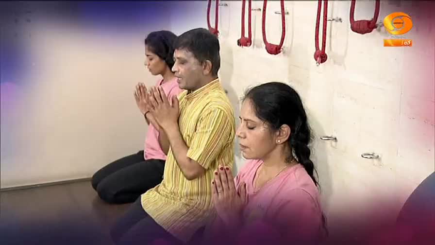 Three people kneel with their hands pressed together in prayer. The man in the center wears a yellow and white striped shirt, while the women on either side wear pink. This scene is from a DD Chandana broadcast in India. Three people kneel with their hands pressed together in prayer. The man in the center wears a yellow and white striped shirt, while the women on either side wear pink. This scene is from a DD Chandana broadcast in India.