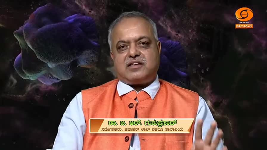 A man in an orange vest speaks directly to the camera. Behind him, a purple, amorphous shape floats against a dark, nebulous background. The DD Chandana logo is visible in the upper right corner. A man in an orange vest speaks directly to the camera. Behind him, a purple, amorphous shape floats against a dark, nebulous background. The DD Chandana logo is visible in the upper right corner.