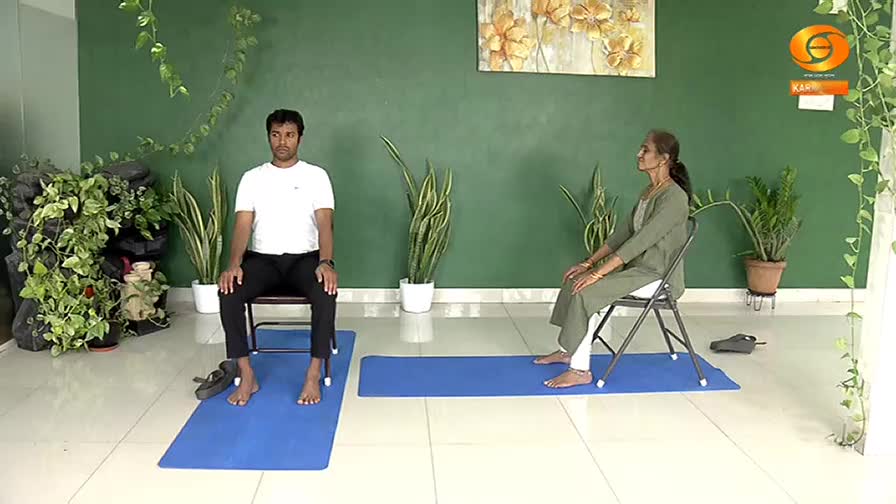 A man and a woman sit on chairs, each on a blue mat, in a studio setting. Their posture suggests a moment of calm, perhaps during a yoga session broadcast on DD Chandana. A man and a woman sit on chairs, each on a blue mat, in a studio setting. Their posture suggests a moment of calm, perhaps during a yoga session broadcast on DD Chandana.