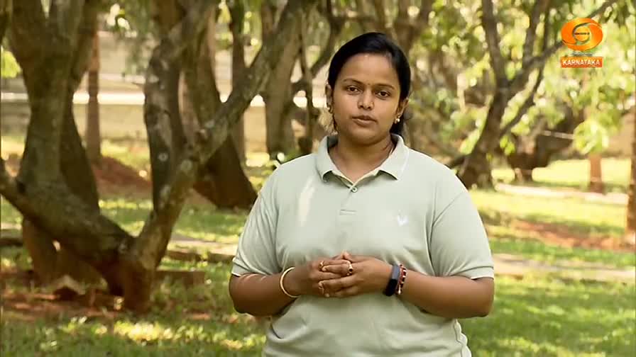 A woman stands in a park, her hands clasped in front of her. The Karnataka logo is visible in the upper right corner.