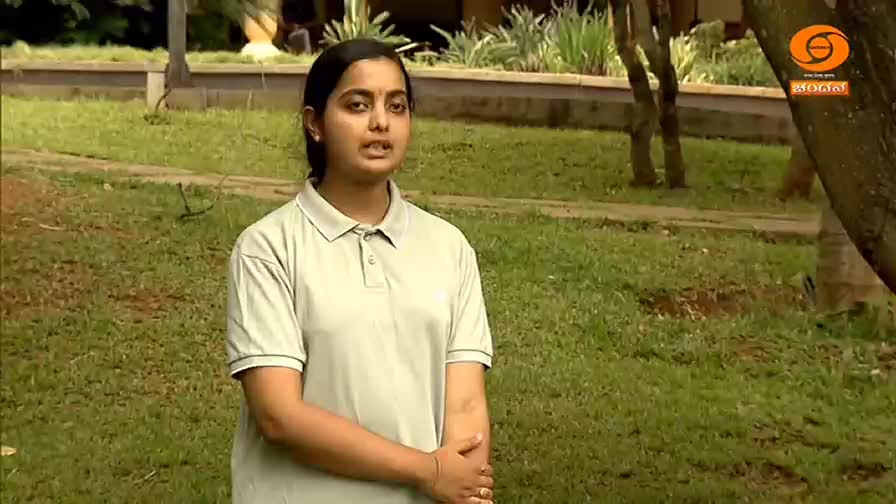 A young woman stands in a grassy area, speaking into a microphone. The DD Chandana logo is visible in the upper right corner.