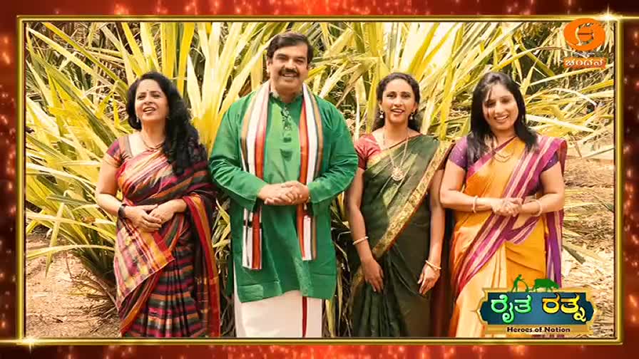 A man in a green kurta and white dhoti stands with three women in colorful sarees, all smiling. They are posing in front of tall, yellowing foliage, likely for a program on DD Chandana.