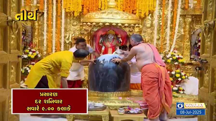 Men in traditional clothing are pouring something white over a large, dark stone. The scene is inside a temple, with a golden idol visible in the background.
