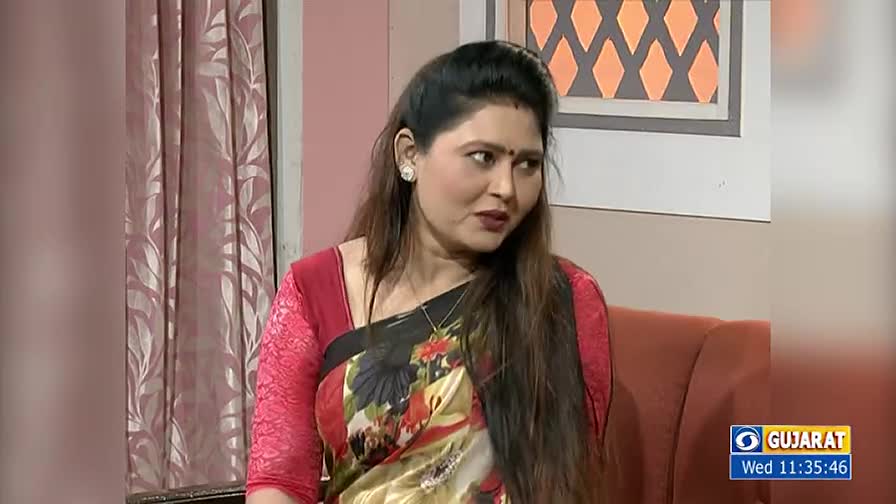 A woman in a floral sari and red sleeves is seated, looking slightly to her left. The DD Girnar logo and the time are in the lower right corner.
