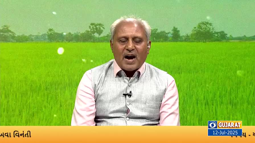 A man in a vest and pink shirt speaks intently, his mouth wide open. Behind him, a bright green field stretches toward a hazy horizon, likely a broadcast from DD Girnar.
