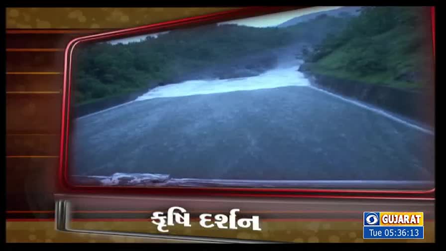 Water gushes forcefully from a dam, a white torrent against the dark green hills. The scene is framed within a television screen, likely a segment from DD Girnar, India.
