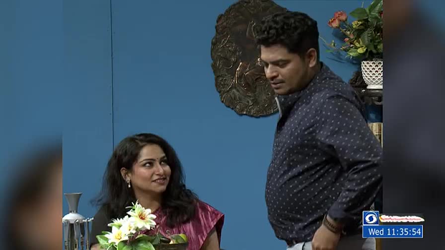 The woman smiles, looking up at the man who seems to be speaking. He's turned towards her, his hands at his sides.

