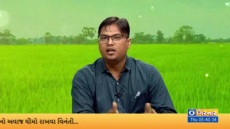 A man in glasses gestures with his hands, speaking directly to the camera against a backdrop of a lush green field. The DD Girnar logo and a time stamp are visible in the lower right corner.

