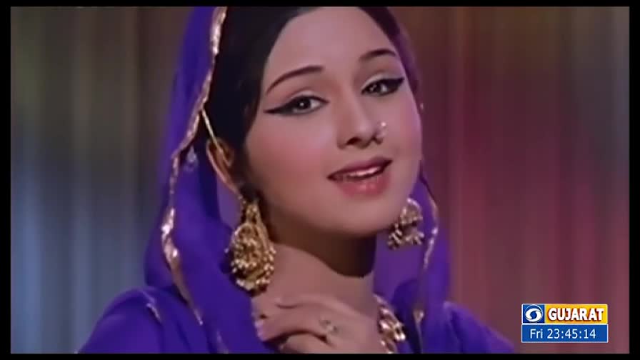 A woman in a purple headscarf and ornate earrings smiles at the camera. The DD Girnar logo and time stamp in the corner suggest this is a broadcast from Gujarat.
