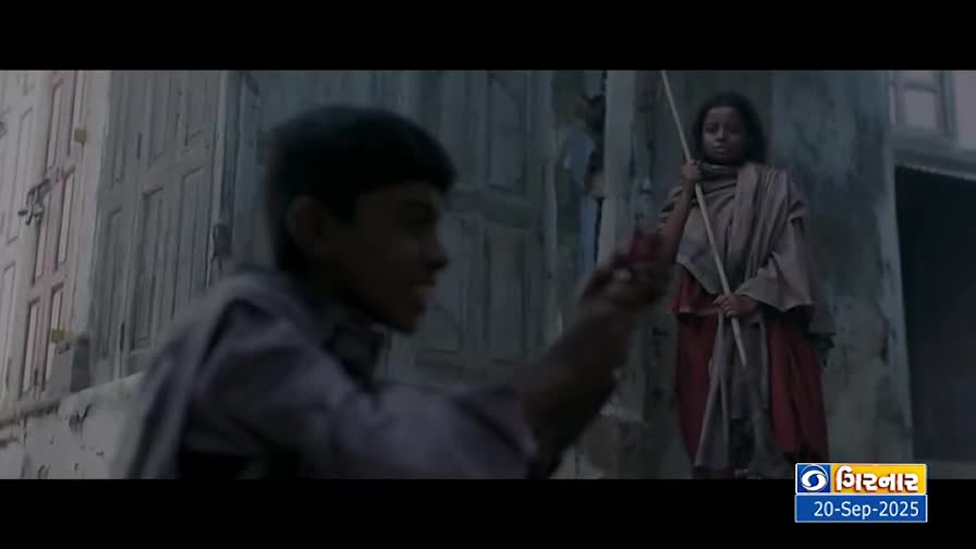 A boy gestures with his hand, seemingly talking to a girl who holds a long stick. She stands still, wrapped in a shawl, as if waiting.
