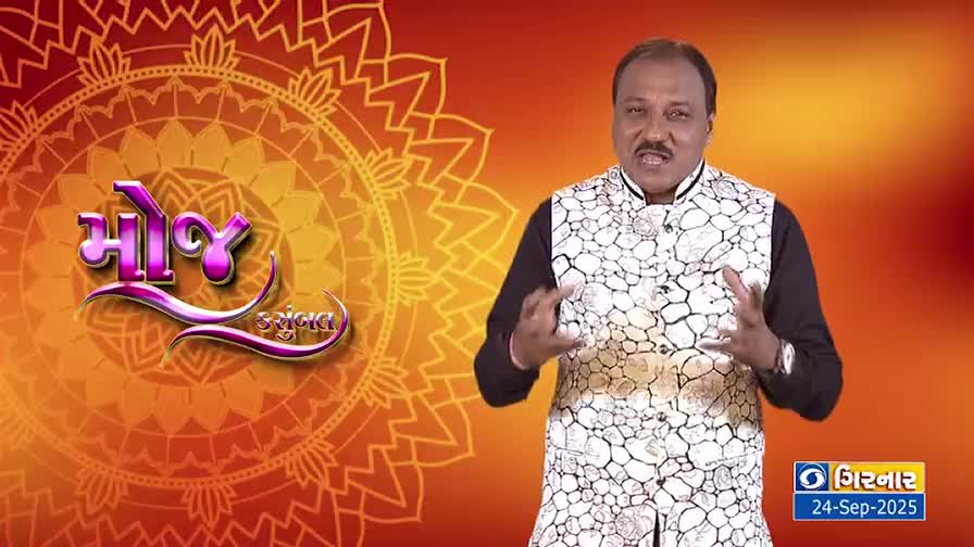 A man in a patterned vest gestures with his hands, speaking directly to the camera. Behind him, a logo for a DD Girnar program is set against a warm, decorative backdrop.
