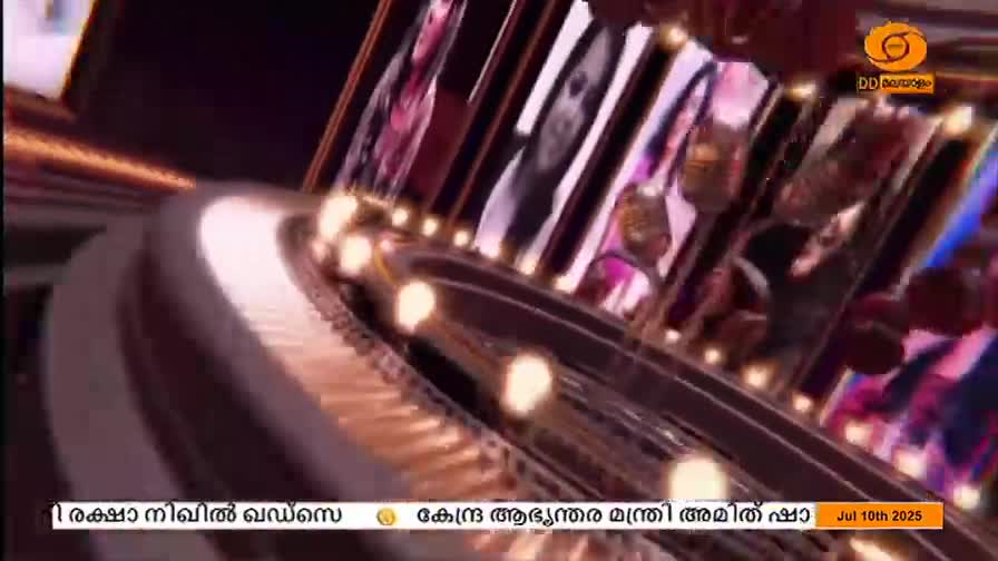 A rotating, circular structure with lights and images of people is in the foreground. The DD Malayalam logo is visible in the top right corner, with text in Malayalam below.
