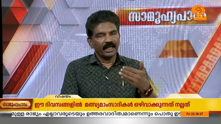 A man with a mustache gestures with his right hand while speaking. The DD Malayalam studio backdrop is a neutral gray with a red and orange banner.

