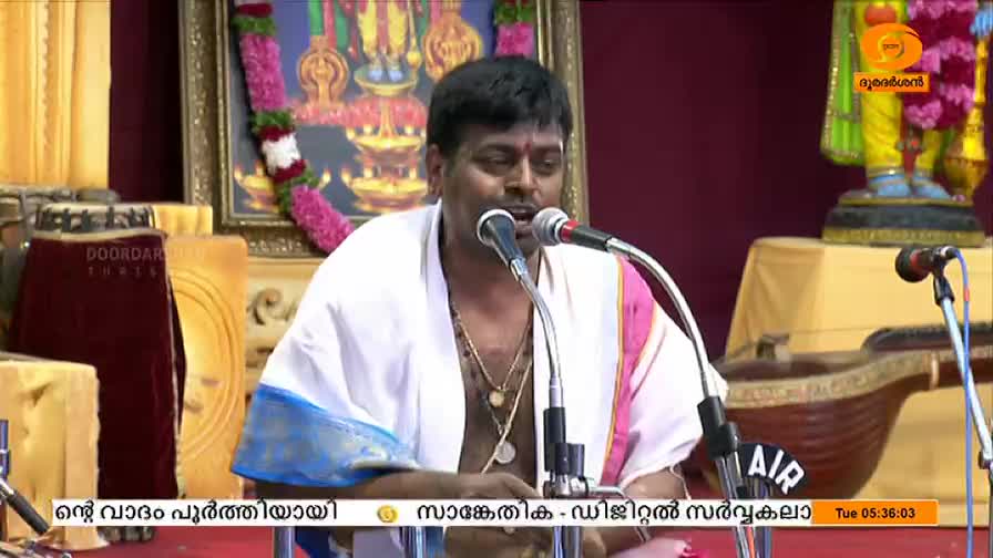 A man in a white shawl speaks into two microphones, his expression animated. The backdrop features religious imagery and the DD Malayalam logo is visible.

