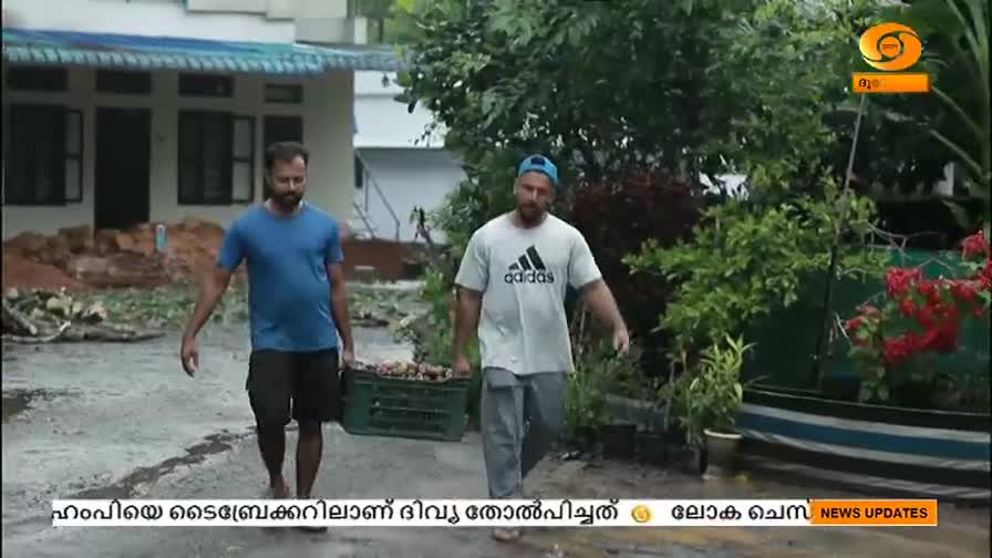 Two men walk toward the camera, one carrying a green crate filled with something, likely debris. The scene is set outside a house, and the DD Malayalam logo is visible in the corner.
