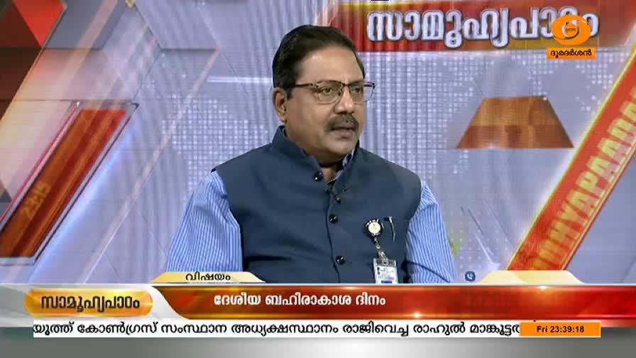 A man in glasses and a dark vest speaks into the camera on DD Malayalam. The broadcast features a scrolling headline in Malayalam, with a graphic that reads "National Space Day."
