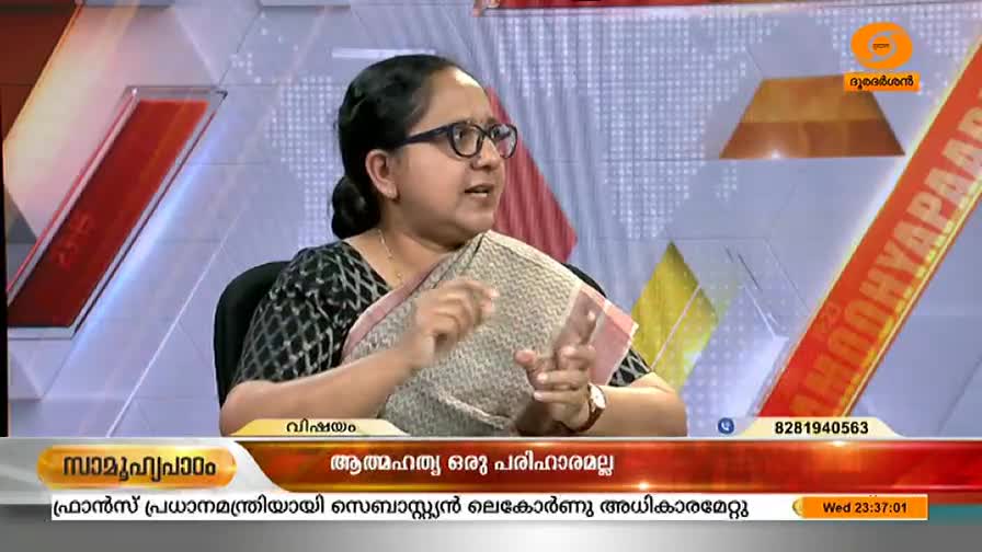 A woman wearing glasses and a sari gestures with her hands while speaking. The DD Malayalam logo and text in Malayalam are visible on the screen.
