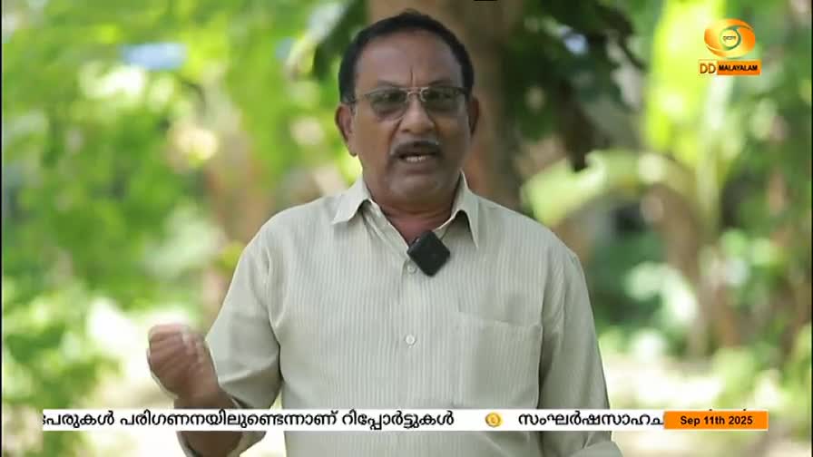 The man in the light shirt gestures with his left hand as he speaks, a small microphone clipped to his collar. The DD Malayalam logo is visible in the corner, and a date is displayed at the bottom of the screen.
