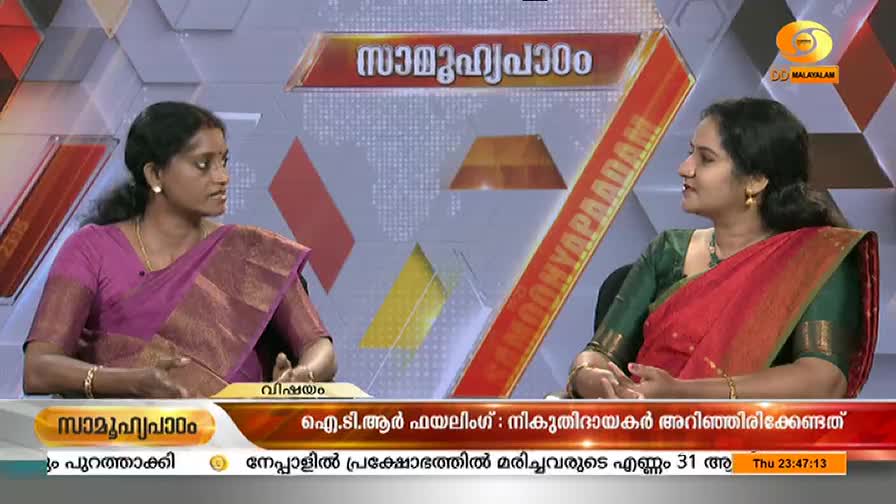 Two women in saris are seated at a table, conversing on a DD Malayalam program. A graphic with Malayalam text and the DD Malayalam logo is displayed on the screen.
