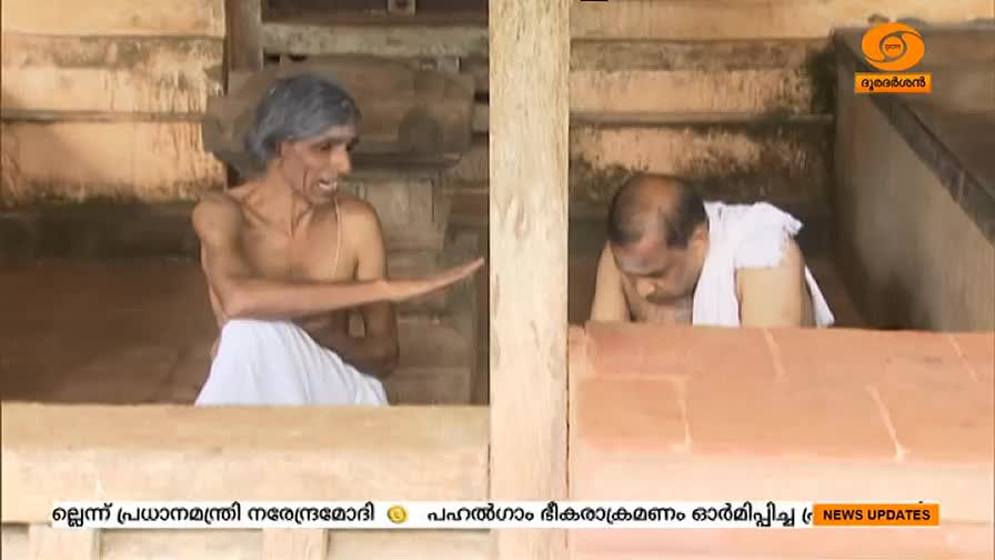 A man with grey hair gestures with his right hand, while another man bows his head, both inside a stone structure. The DD Malayalam logo is visible in the corner.
