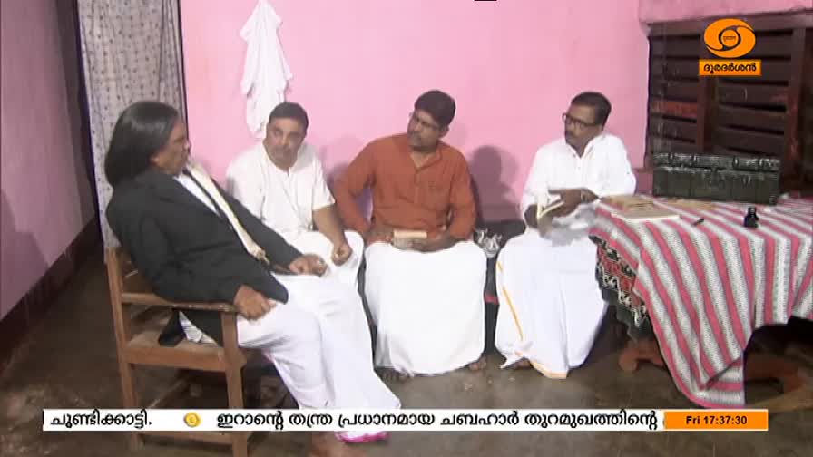 Four men sit in a room, one in a suit, the others in white and orange shirts, engaged in conversation. The DD Malayalam logo is visible in the corner, indicating a broadcast from India.
