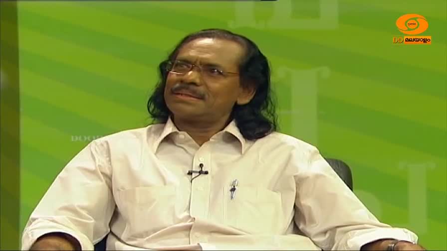 A man in a white shirt sits, looking slightly off-camera, with a DD Malayalam logo visible in the corner. He's in a studio setting, against a green striped backdrop.
A man in a white shirt sits, looking slightly off-camera, with a DD Malayalam logo visible in the corner. He's in a studio setting, against a green striped backdrop.