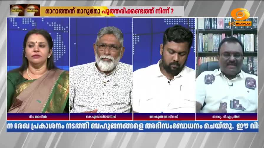 Four people are seated, facing forward, in what appears to be a television studio. The backdrop is a blue screen with a grid pattern, and a logo for DD Malayalam is visible in the upper right corner.