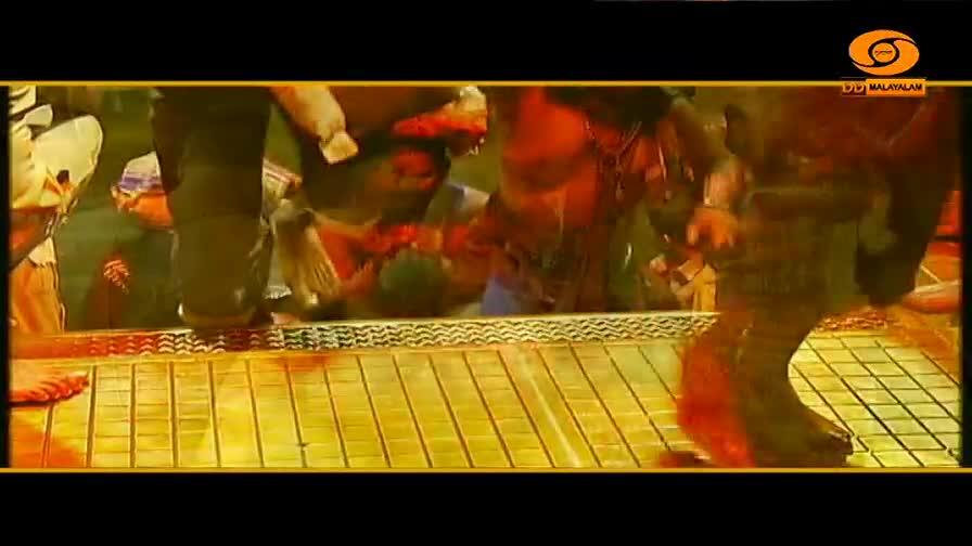 A crowd surges forward, their feet shuffling on a golden, tiled surface. The DD Malayalam broadcast captures the intense energy of the moment.