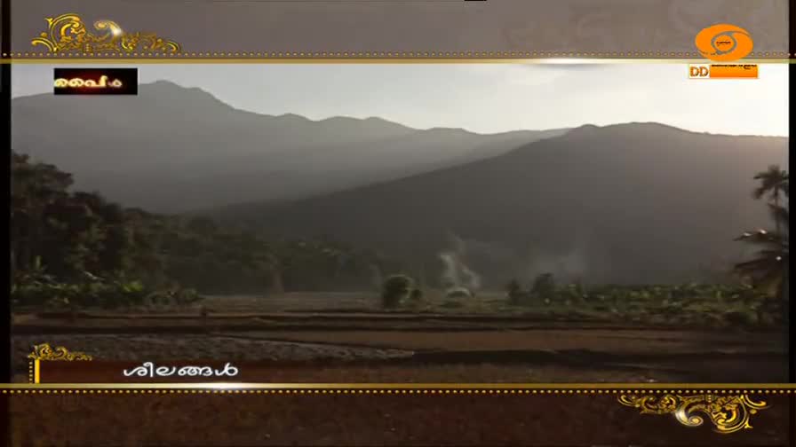 Mist rises from the fields below the hazy mountains. A small, dark rectangular graphic with Malayalam text hovers in the upper left corner, and the DD Malayalam logo appears in the upper right.