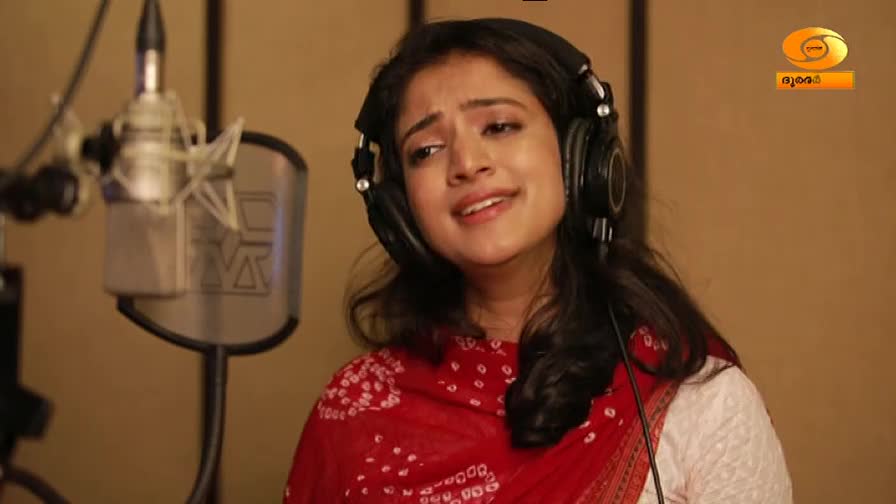 A woman with headphones on sings into a microphone in a studio. The DD Malayalam logo is visible in the corner.
