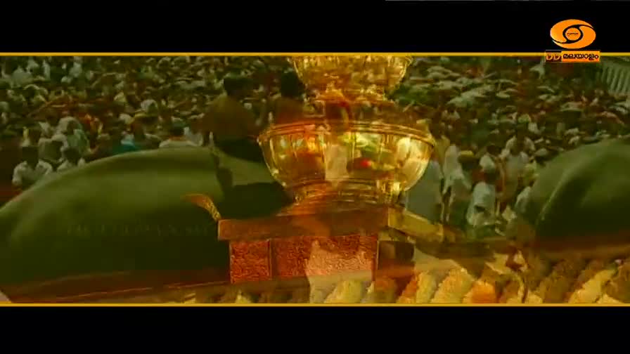 A massive, decorated elephant moves slowly through a dense crowd. A golden shrine, likely carrying a deity, is perched on its back.