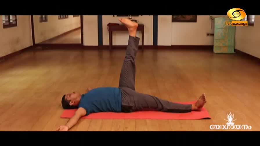 A man is lying on a red mat, his left leg extended flat on the floor while his right leg is raised straight up. He's on a wooden floor in what looks like a studio, with a DD Malayalam logo visible in the corner.