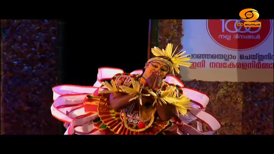 A dancer, adorned in vibrant traditional attire, bows with hands pressed together. Their elaborate headdress, made of yellow fronds, fans out around their face.