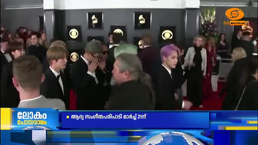 A group of young men in sharp suits walk past, some with brightly colored hair. A DD Malayalam chyron scrolls across the bottom of the screen. A group of young men in sharp suits walk past, some with brightly colored hair. A DD Malayalam chyron scrolls across the bottom of the screen.