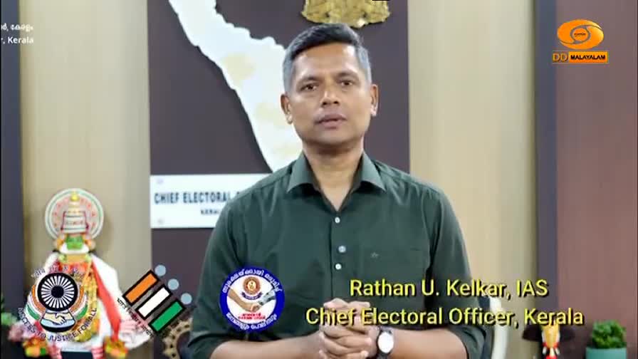 A man in a dark green shirt stands before a map of Kerala. He's identified as Rathan U. Kelkar, IAS, Chief Electoral Officer, Kerala, with the DD Malayalam logo visible.