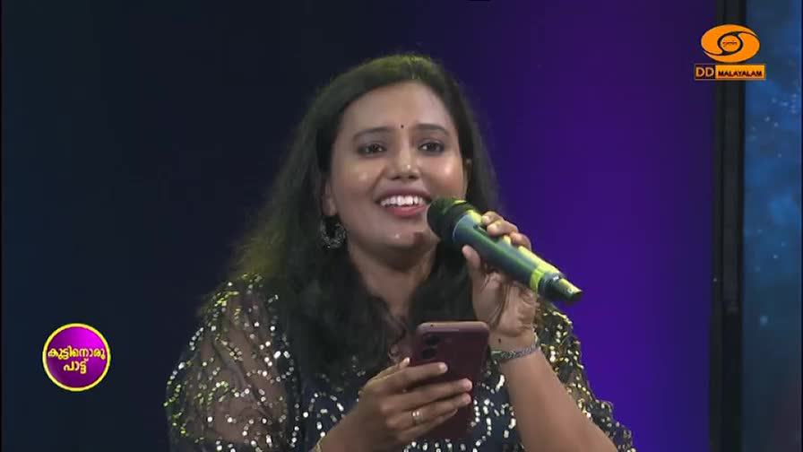 A woman sings into a microphone, her phone held in her other hand. The DD Malayalam logo is visible in the corner.